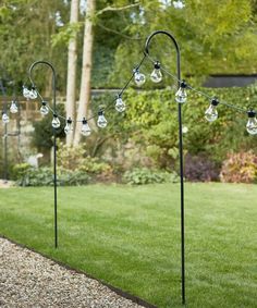 three black poles with clear glass balls hanging from them in the middle of a garden