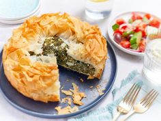 a blue plate topped with a piece of pie next to a bowl of salad and fork