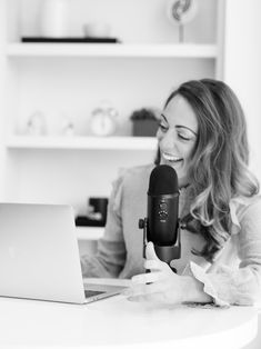 a woman sitting in front of a laptop computer holding a microphone