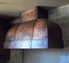 an old fashioned stove hood mounted on the side of a stone wall in a kitchen