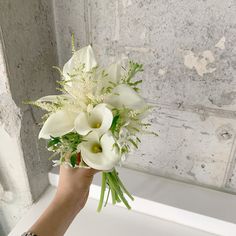 a woman's hand holding a bouquet of white flowers in front of a wall