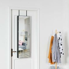 an open door to a white room with clothes hanging on the rack and a chair in the background