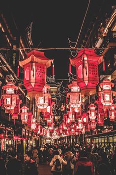 people are walking down the street at night with red lanterns hanging from the buildings above them