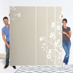 two people standing behind a wall with white flowers on it and one person holding up the wall