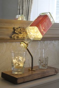 a light that is on top of a wooden shelf next to two glasses and a bottle