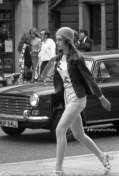 a woman crossing the street in front of a car and people walking on the sidewalk