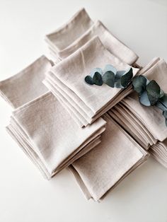 a stack of folded linen napkins with eucalyptus leaves on top and one green leaf sticking out of the middle