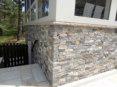 a stone wall next to a building with chairs on the front and back porch area