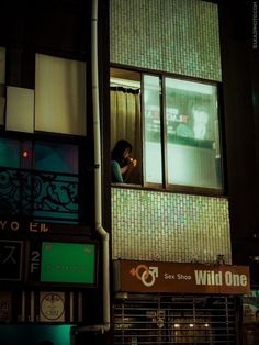 a woman standing in the window of a building at night