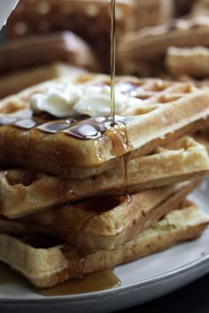 a stack of waffles on a plate with syrup being drizzled over them