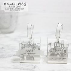 two clear square tags with silver foil on them that say home for christmas and season of joy