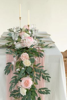 the table is set with pink and white flowers, greenery, candles and napkins