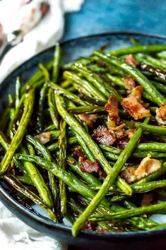 cooked green beans with bacon in a black bowl on a blue tablecloth and white napkin