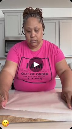 a woman in a pink shirt is making something out of paper on a counter top