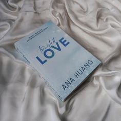 a book sitting on top of a bed covered in white sheets and satin material with the words love written above it