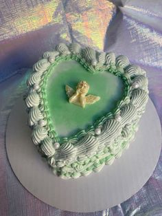 a heart shaped cake with green frosting and a small gold angel decoration on top