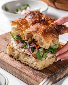 a person is holding up a sandwich on a cutting board