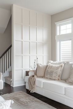 a living room filled with white furniture and pillows on top of a rug in front of a window