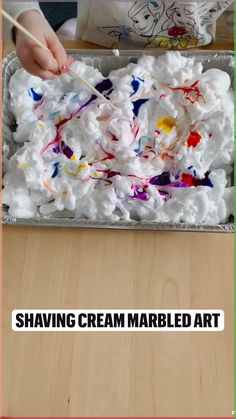 a child is painting with white and red paint on a sheet of paper that says shaving cream marbled art