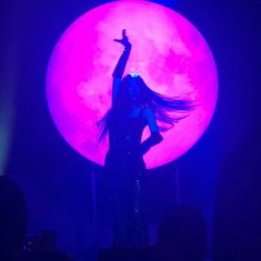 a woman with long hair standing in front of a large pink moon on stage at night