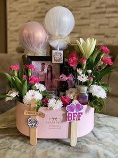 an arrangement of flowers and photos in a pink basket