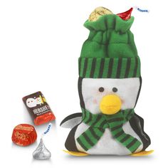 a stuffed penguin with a green hat and scarf next to some chocolate candies on a white background