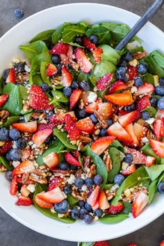 a white bowl filled with spinach, strawberries and blueberries on top of a table