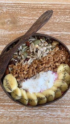 a bowl filled with granola, yogurt, and other toppings next to a wooden spoon