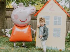 a little boy standing next to a large inflatable peppo pig house and balloon