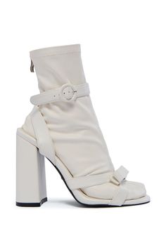 The AZALEA WANG Quinlan White Sandal Bootie is a unique hybrid style featuring a stretchy, removable faux leather sock with an ankle-high shaft, tonal stitching, and a tonal inner ankle zipper closure. The coordinating faux leather sandal features a chunky block heel, an almond toe silhouette, dual bow-adorned toe bands, and a textured rubber outsole. Complete with a wrap-around ankle strap and circular buckle detailing.  (all measurements are approximate from size 7.5) - Faux Leather Upper - Almond Toe - Chunky Heel - Ankle-High Shaft - 4.5” Heel Height - 12.5” Sock Shaft Length - Imported  Product ID: 428685 Sock Bootie, White Sandal, Azalea Wang, Leather Socks, Chunky Block Heels, White Sandals, White Sock, Chunky Heels, Leather Sandals