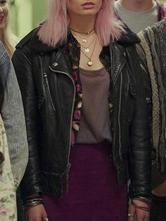 a woman with pink hair wearing a black leather jacket and purple skirt standing in front of other people