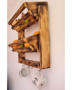 a wooden shelf with two mugs on it and some cups hanging from the wall