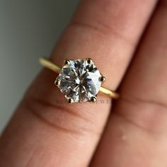 a close up of a person's hand holding a ring with a diamond in it