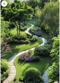 a garden with lots of green grass and flowers on the side of it, along with a path leading to trees