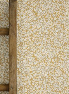 an old wooden ladder leaning against a wall with yellow and white flowered paper on it