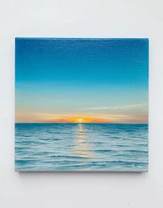 a painting of the sun setting over the ocean on a white wall with blue water