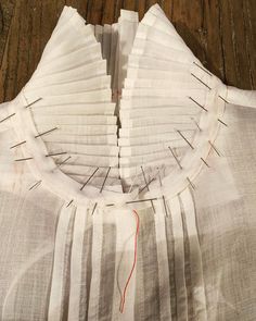 a white shirt with red thread on it sitting on top of a wooden floor next to a pair of scissors