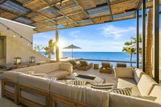 an outdoor living area with couches, tables and umbrellas overlooking the ocean on a sunny day