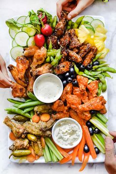 a platter filled with chicken wings, vegetables and dips