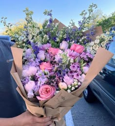 a person holding a bouquet of flowers in front of a blue car on the street