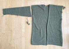 a green knitted sweater laying on top of a wooden floor