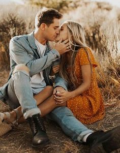 a man and woman sitting on the ground kissing each other in front of some dry grass