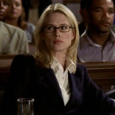 a woman with glasses sitting at a table in front of other people and looking off to the side