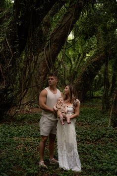 a man and woman standing in the woods holding a baby