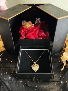 a black box with some red roses in it and a gold heart pendant on the front