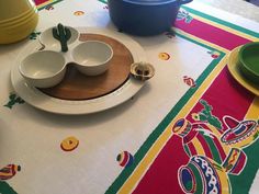 a table topped with plates and bowls on top of a white table cloth covered in colorful designs