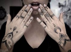 a woman holding her hands up to her face with tattoos on it's fingers