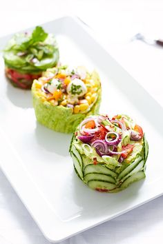 three small cucumbers on a white plate topped with lettuce and tomatoes