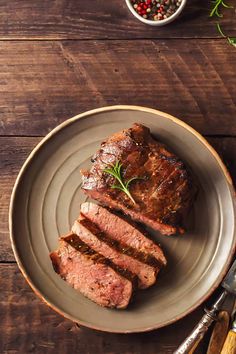 a piece of steak on a plate next to a small bowl of peppercorst