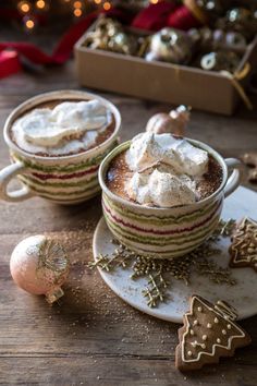 two cups of hot chocolate with whipped cream on top and christmas decorations around the edges